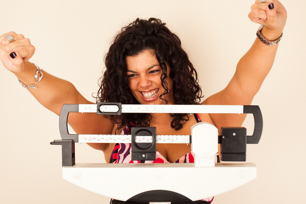 A determined woman showcasing her progress on a weight scale, celebrating her journey towards a healthier lifestyle.